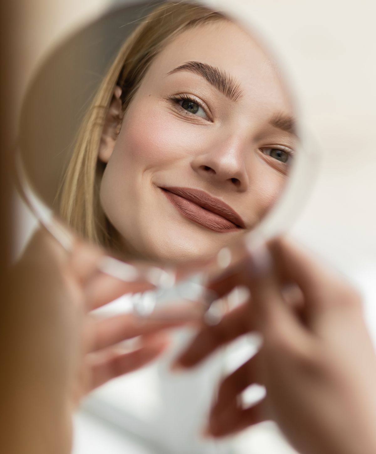 Woman smiling into a mirror, natural makeup look.