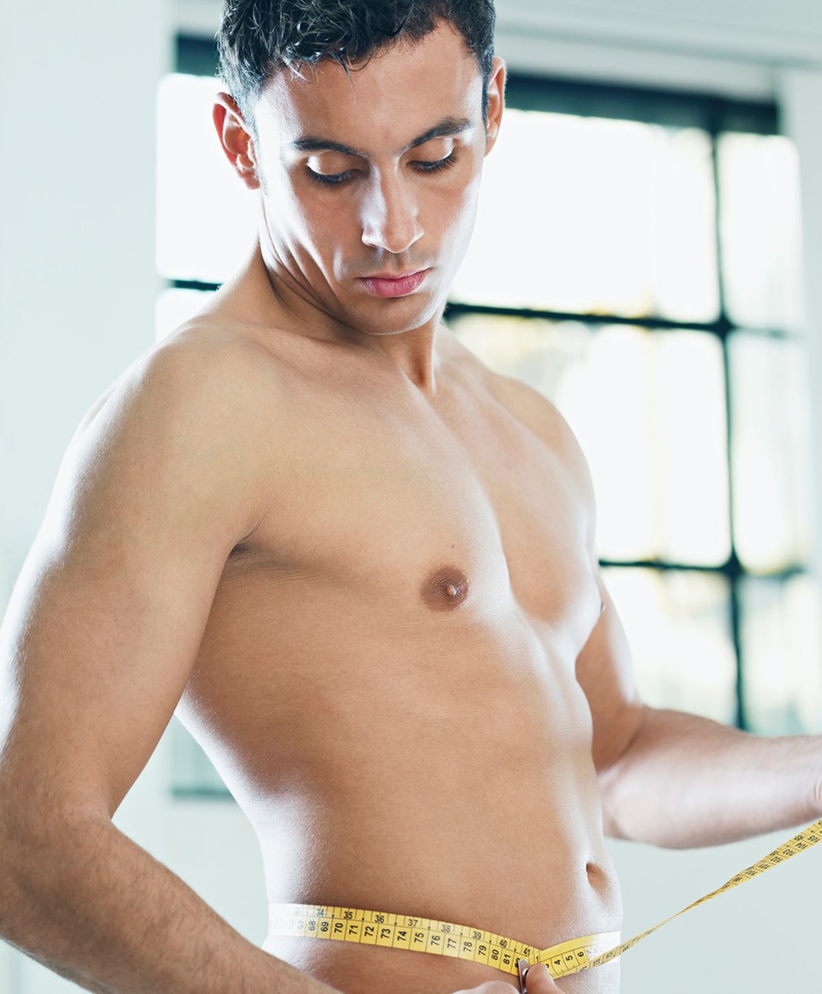 Man measuring his waist with a tape measure.
