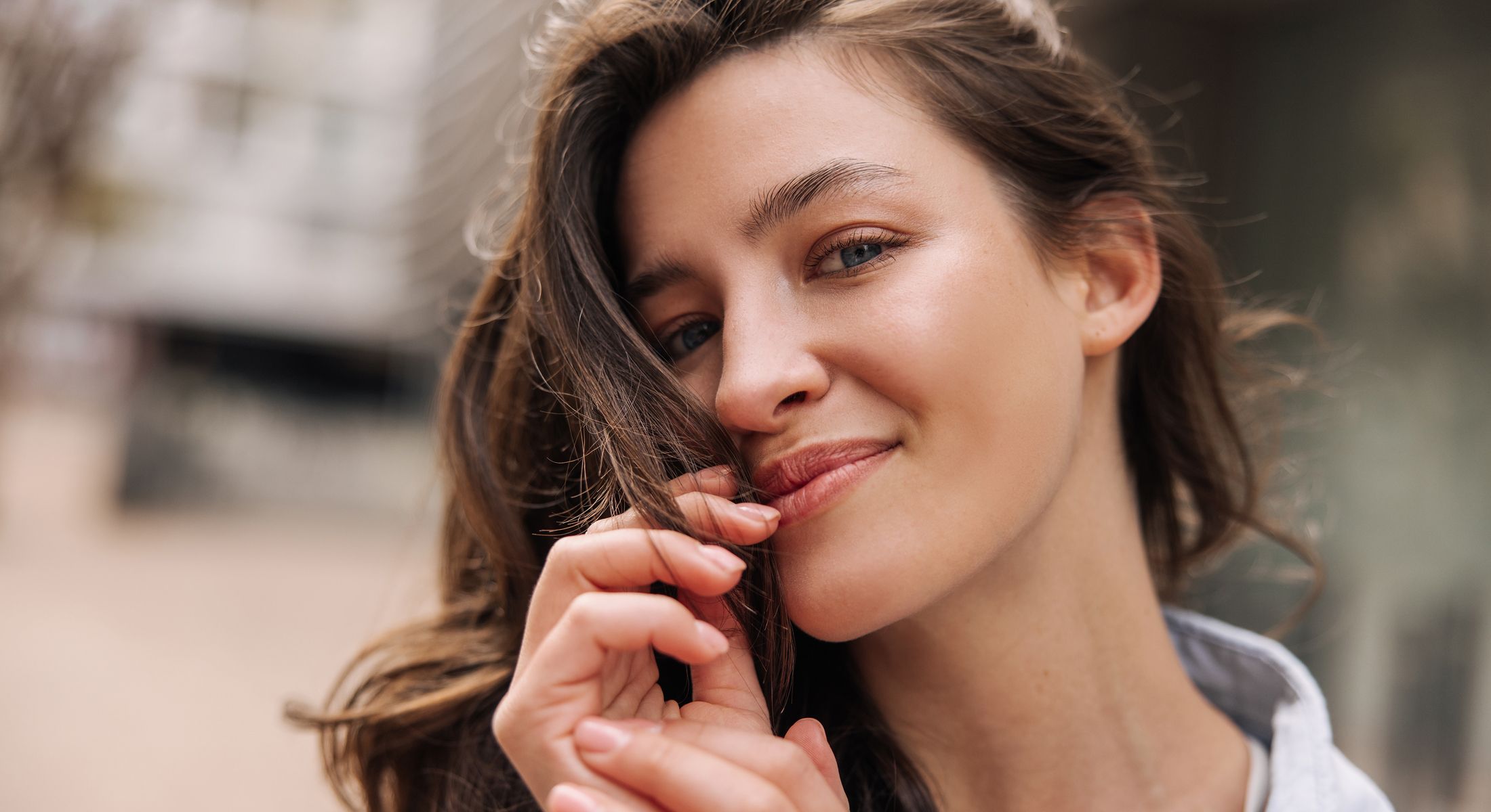 Smiling woman gently touching her hair outdoors.