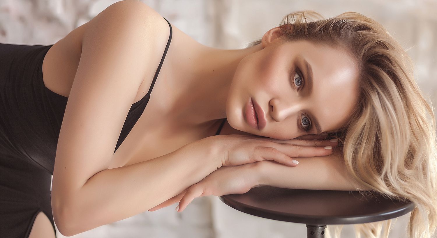Model resting on a stool with soft lighting.